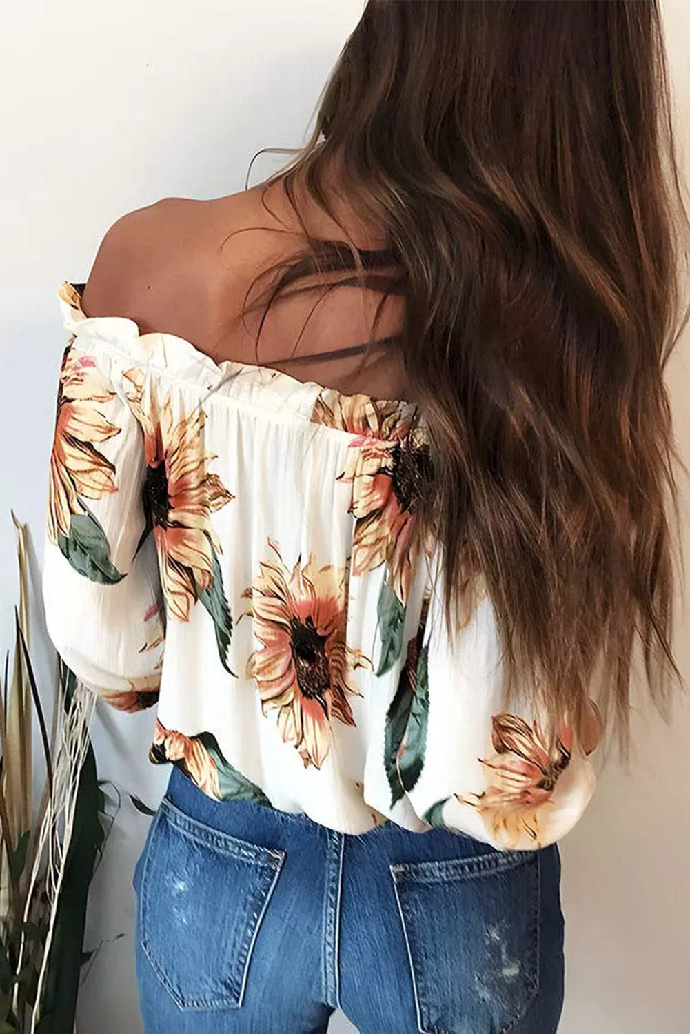 Back view of a woman wearing a floral ruffled tassel tie off shoulder blouse with sunflowers and relaxed jeans.