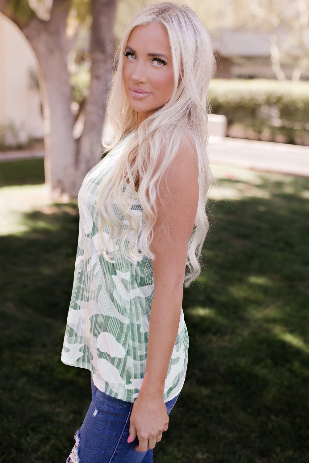 Stylish woman modeling a trendy green camo tank top in a sunny outdoor setting.