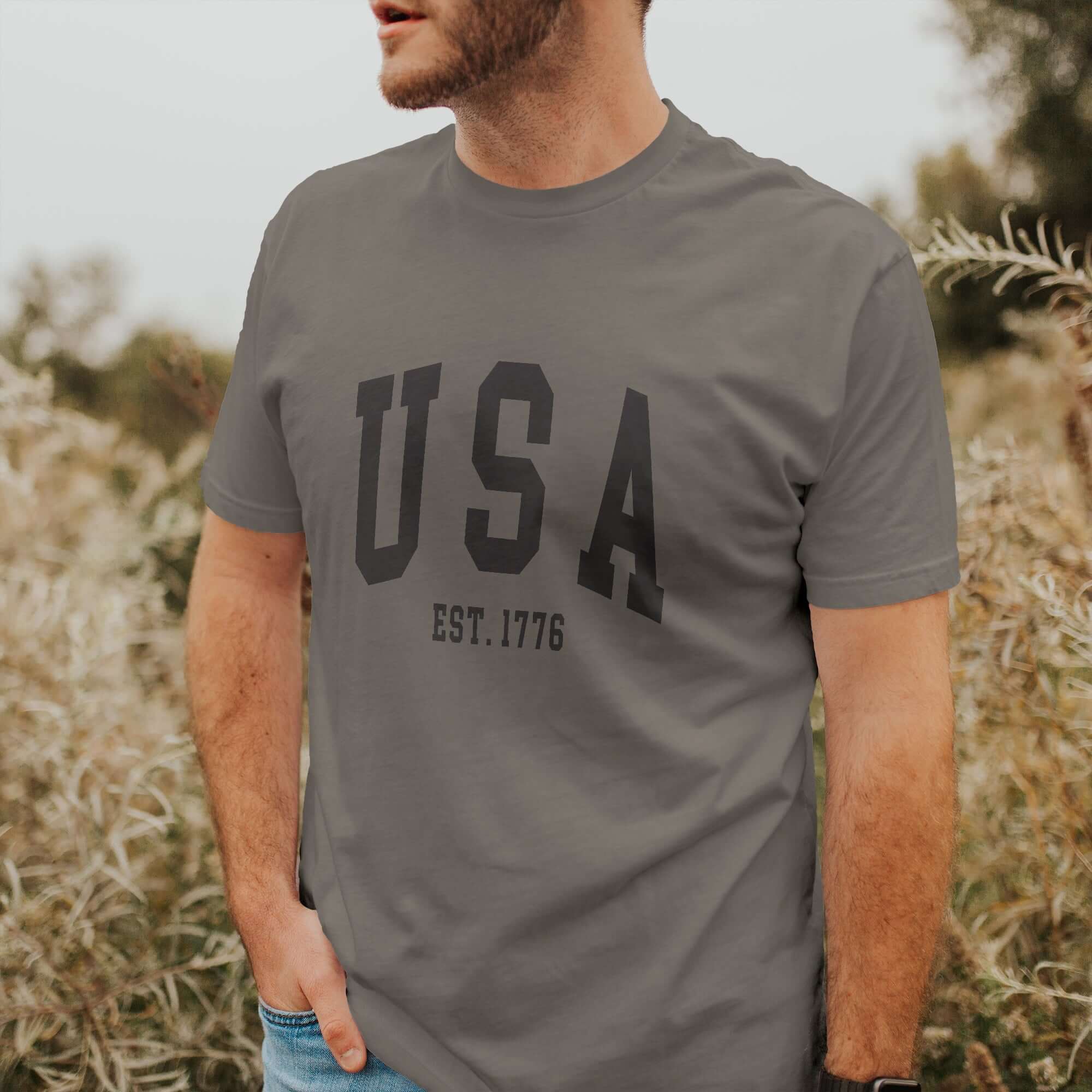 Model wearing USA EST 1776 short sleeve t-shirt in relaxed fit, set against a natural outdoor backdrop.