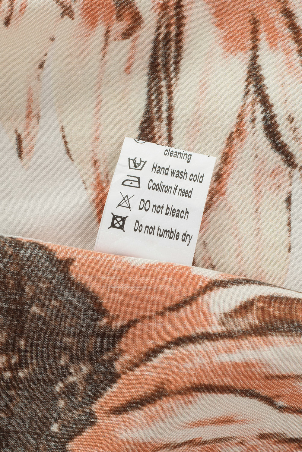 Fabric care label for floral ruffled tassel tie off shoulder blouse, featuring washing instructions and care symbols.