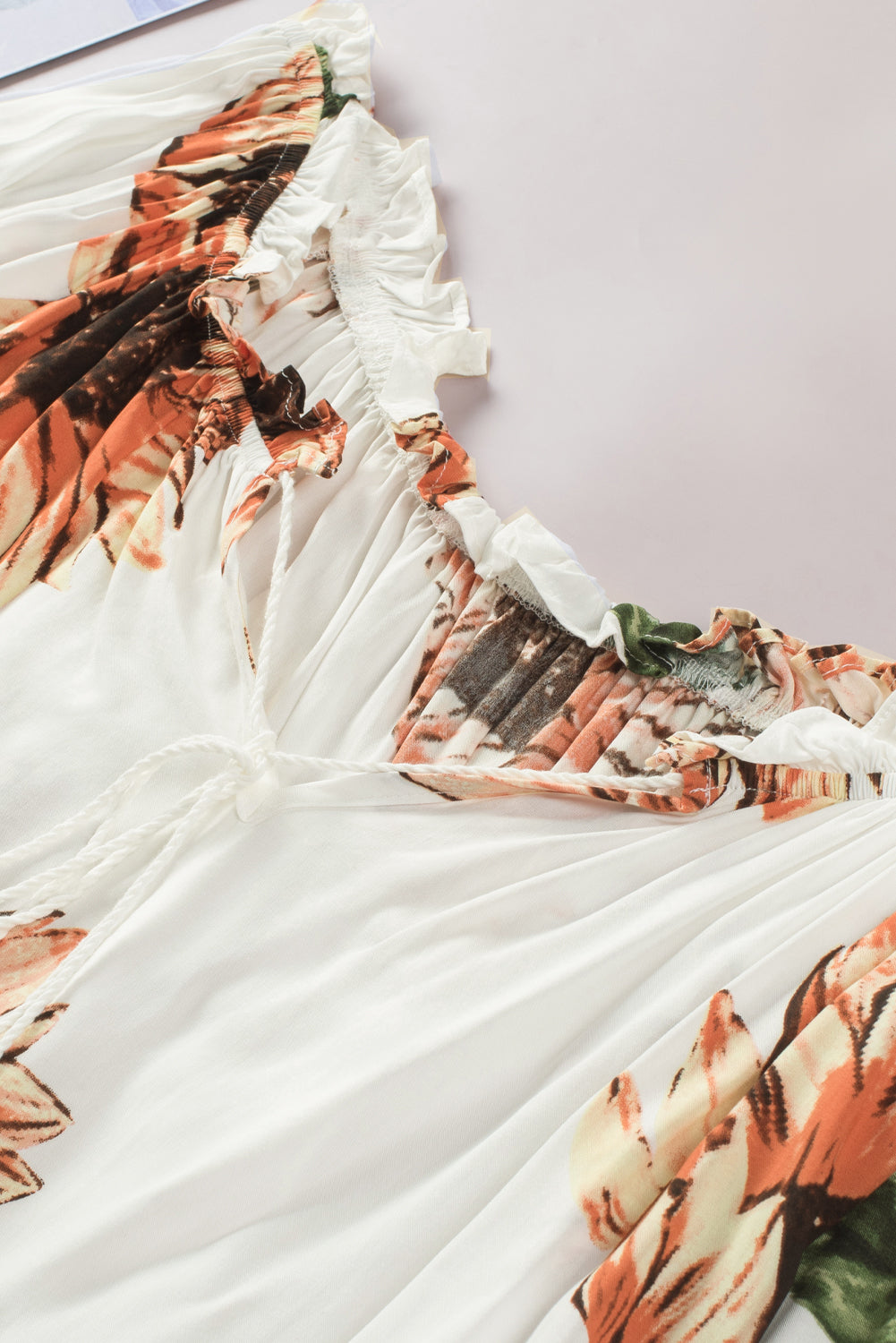 Floral ruffled off shoulder blouse with tassel ties and vibrant sunflowers on a soft white fabric background.