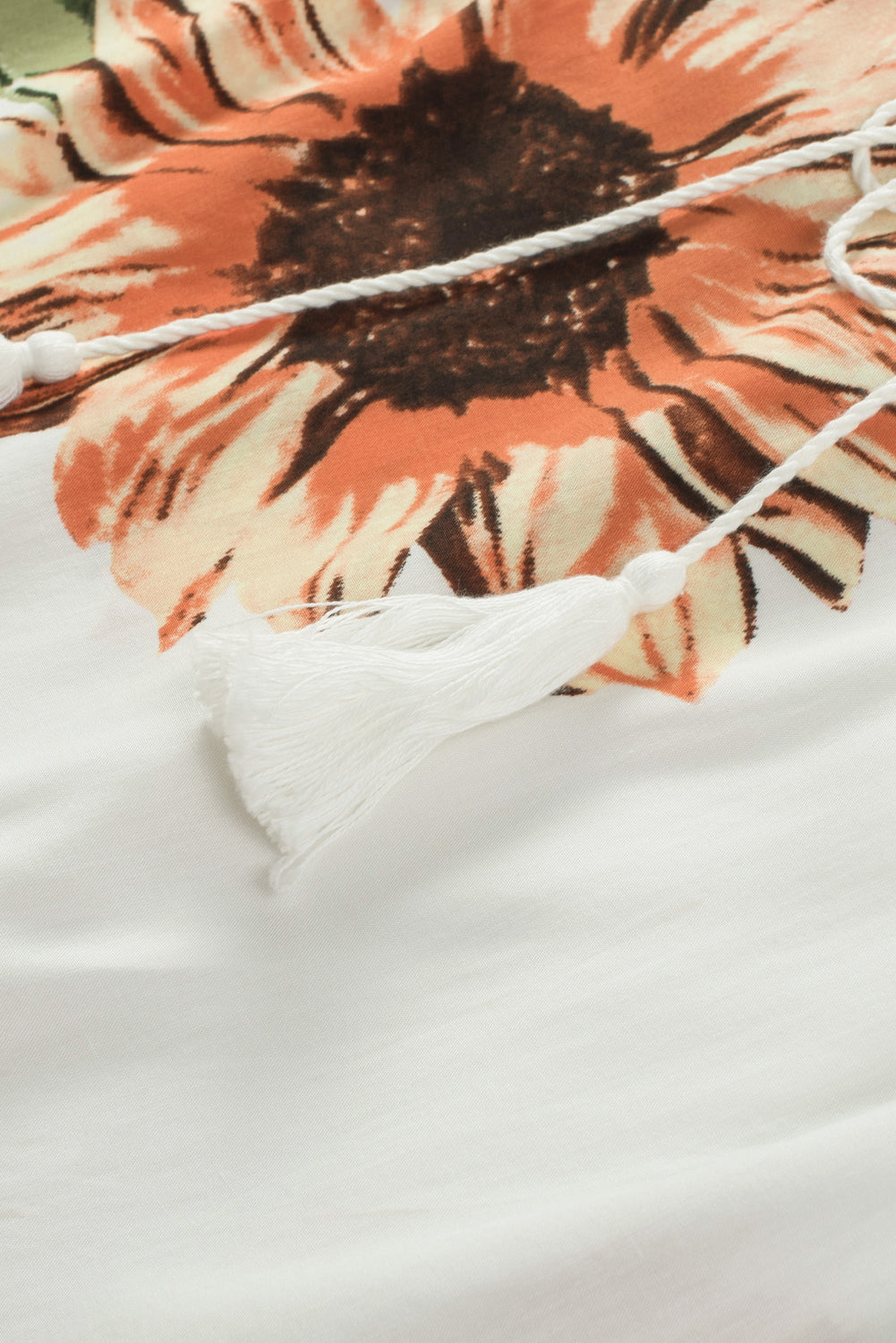 Close-up of floral ruffled blouse featuring sunflowers and white tassel ties.