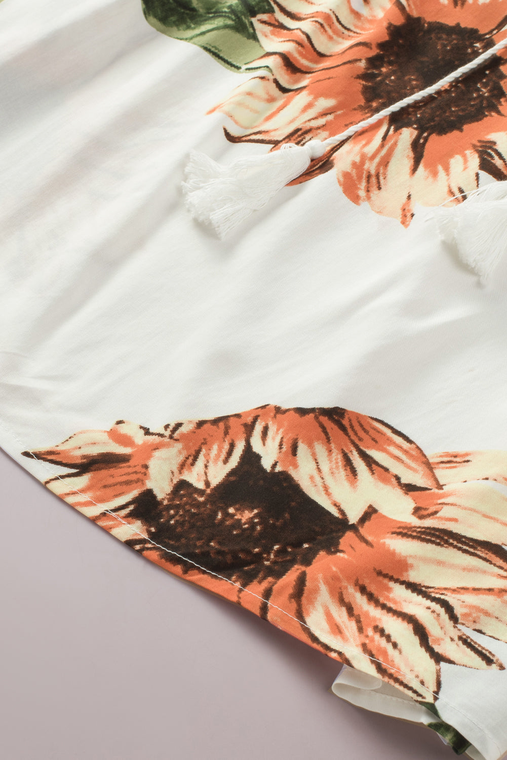Close-up of floral ruffled tassel tie off shoulder blouse featuring vibrant sunflowers on a light fabric.