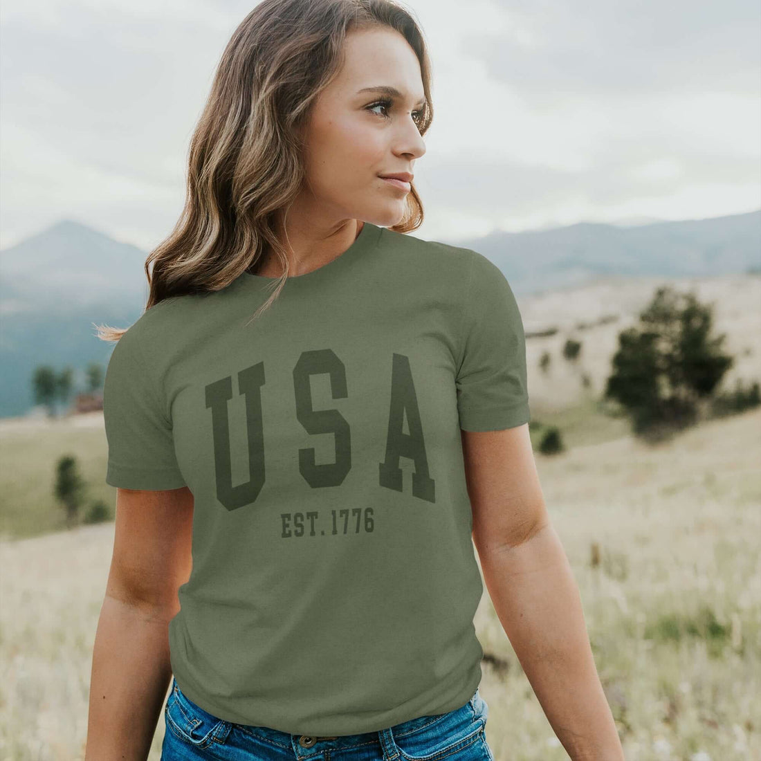 Model in USA Est 1776 short sleeve t-shirt, featuring relaxed fit and distressed design, outdoors in a scenic landscape.