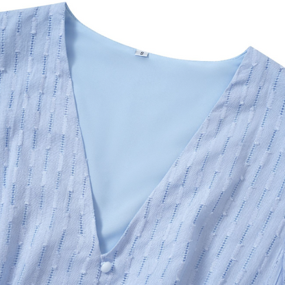 Close-up of a light blue womens v-neck dress showcasing the textured fabric and button detail.