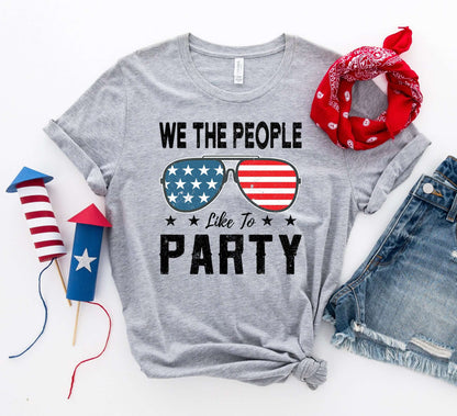 We the People Like to Party T-shirt with patriotic sunglasses design, styled with bandana and festive accents.