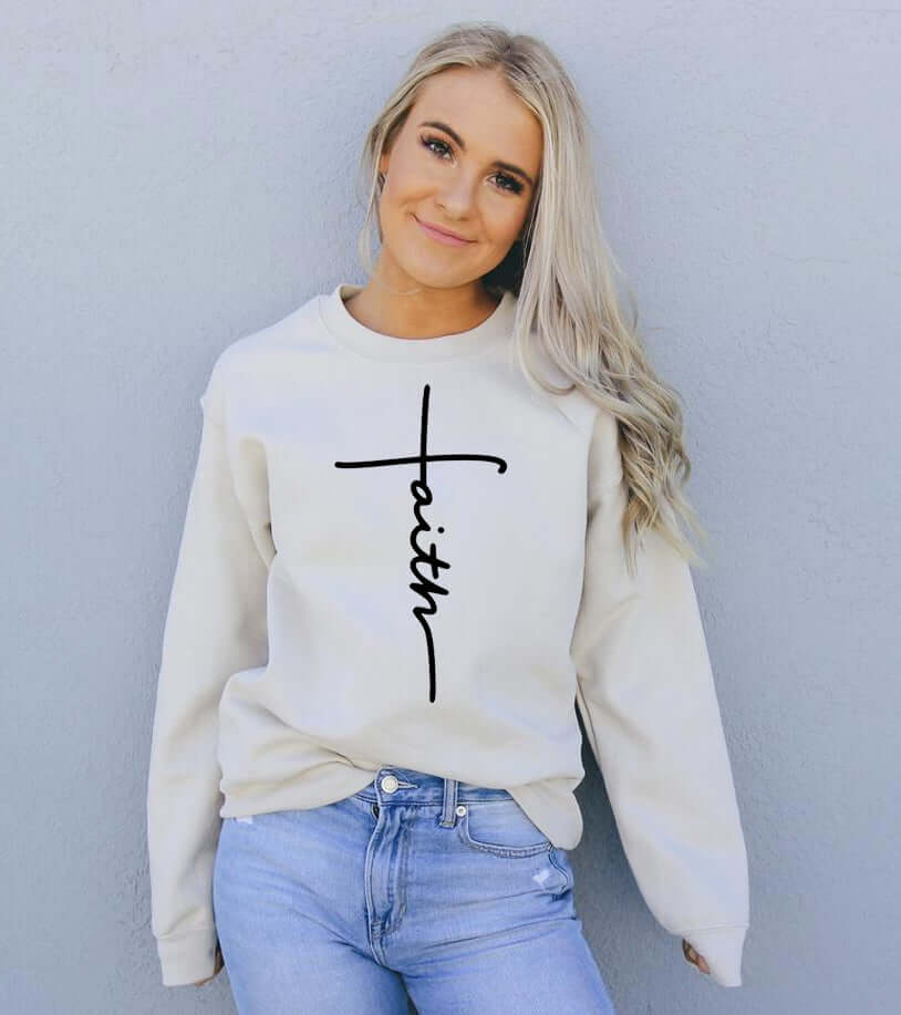 Woman wearing a cream Faith Sweatshirt with a stylish cross design, showcasing casual fashion and comfort.